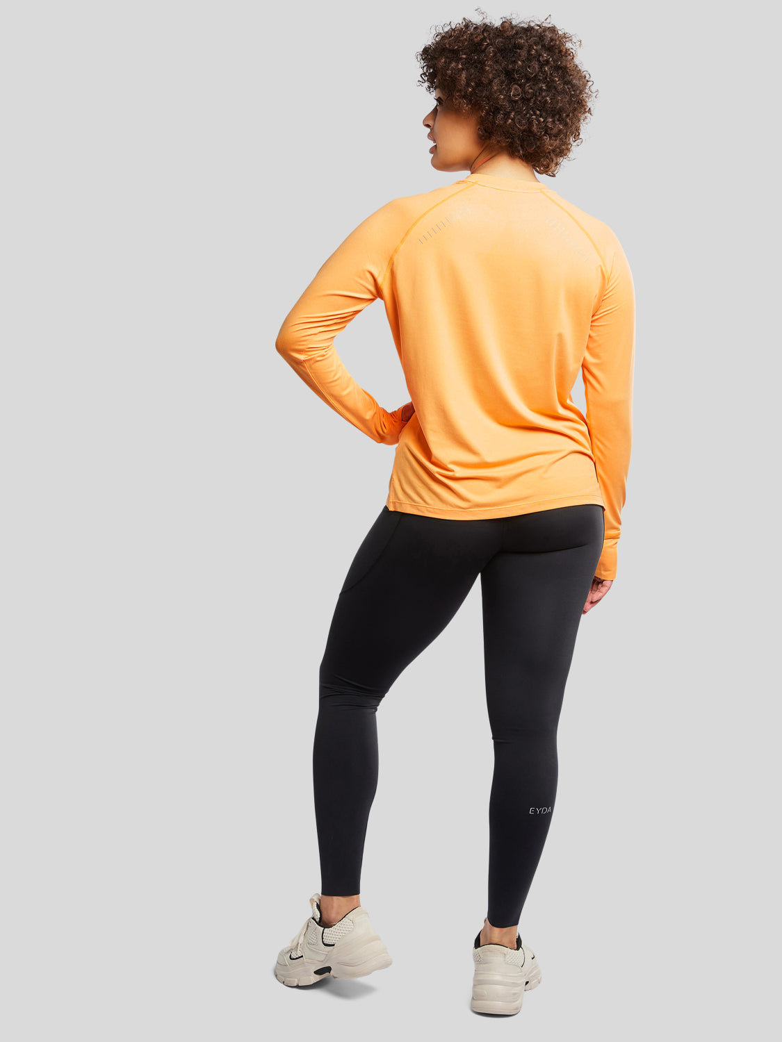 kvinde bagfra med træningstrøje i farven apricot og sorte tights