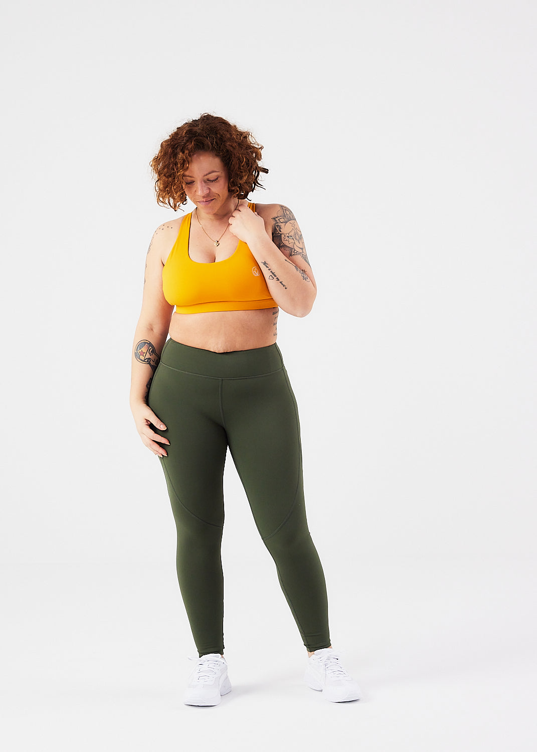 kvinde forfra med sports bh med feminine detaljer i farven sunset og grønne tights